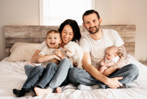 Family photographer, family of four sitting on bed laughing