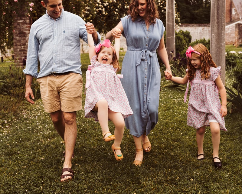 Family photographer, mom and dad swinging little girl between them by her arms