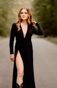 Senior Photographer, woman standing on road touching hair in a black dress