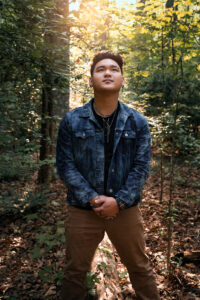 Senior Photographer, Young man standing with his arms crossed in front of him in the forest