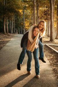 Portrait photographer. 2 women on fall path piggyback