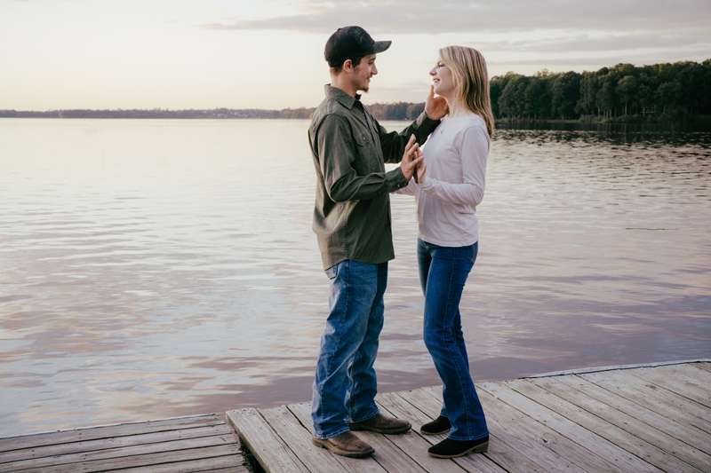 Man and woman standing on dock holding hands at sunset
