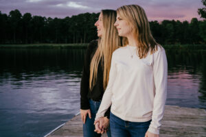 Family photographer. 2 women holding hands standing on a dock looking at sunset