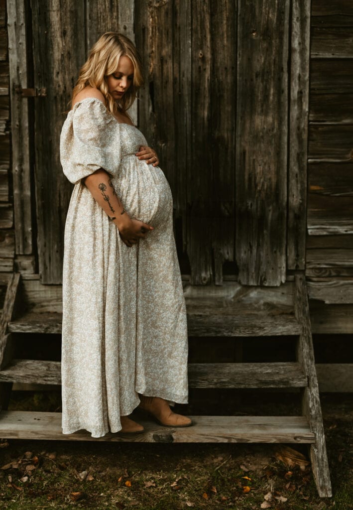 Family photographer, woman in white dress holding belly standing on wooden steps