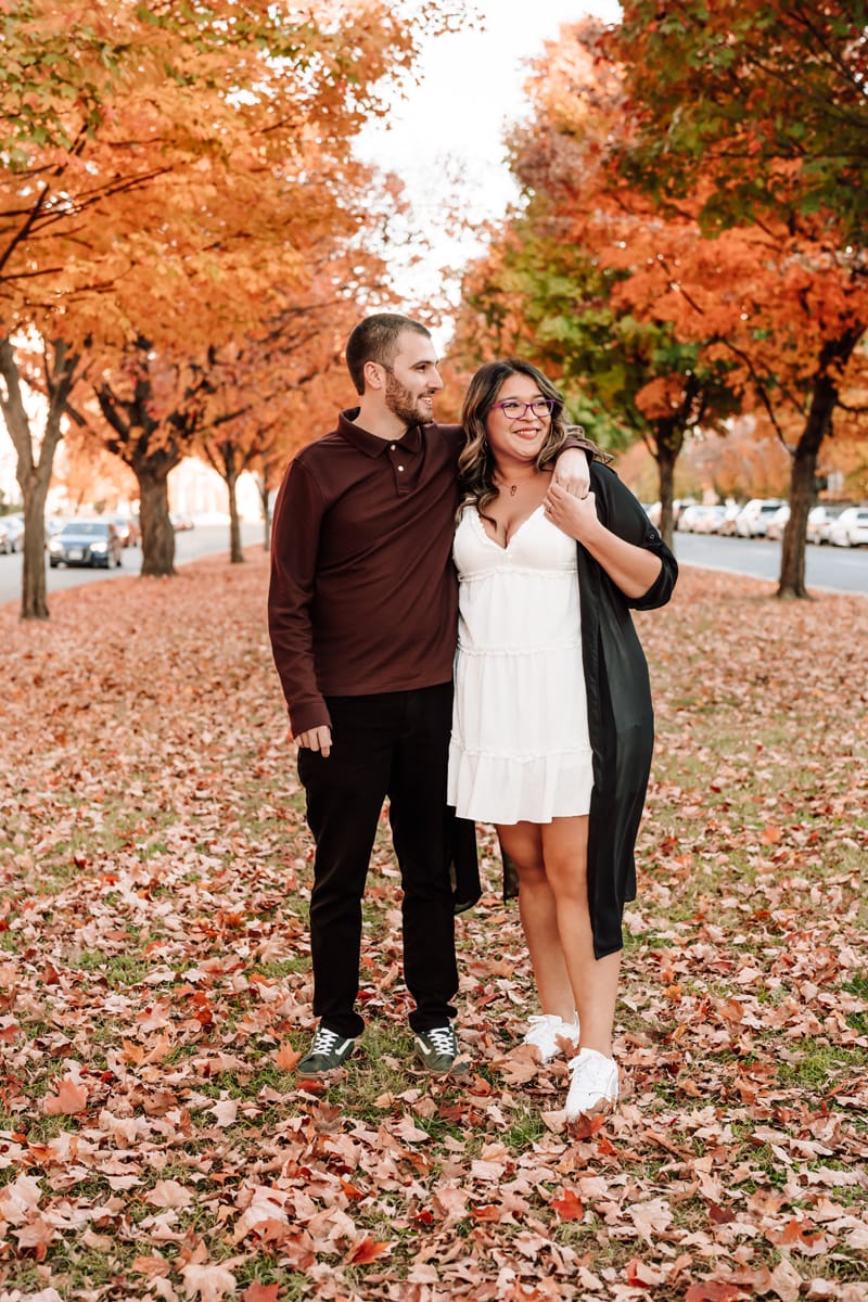 Couples photographer, woman and man with arms over shoulder standing on fall path