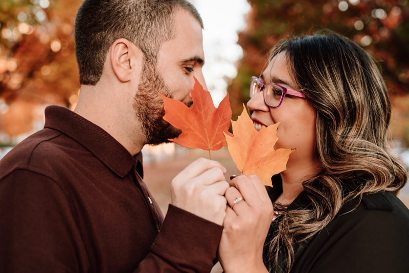 Couples photographer, woman and man holding fall leaves in front of face facing each other