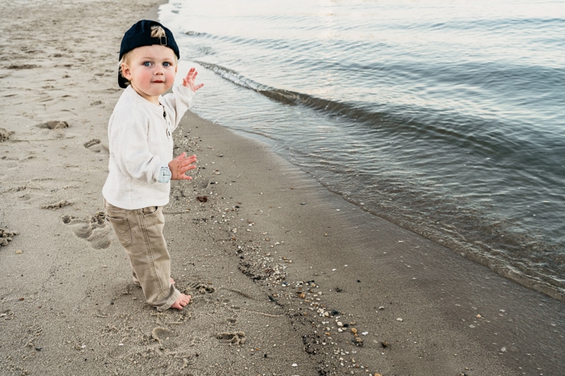 Family photographer, young child standing in sand by ocean