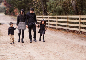 Family photographer, mother and father holding hands with daughter and son walking on dirt road