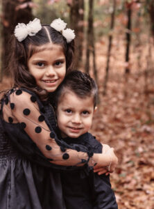Family photographer, sister hugging brother standing in woods