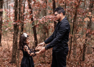 Family photographer, father and daughter holding hands standing in woods